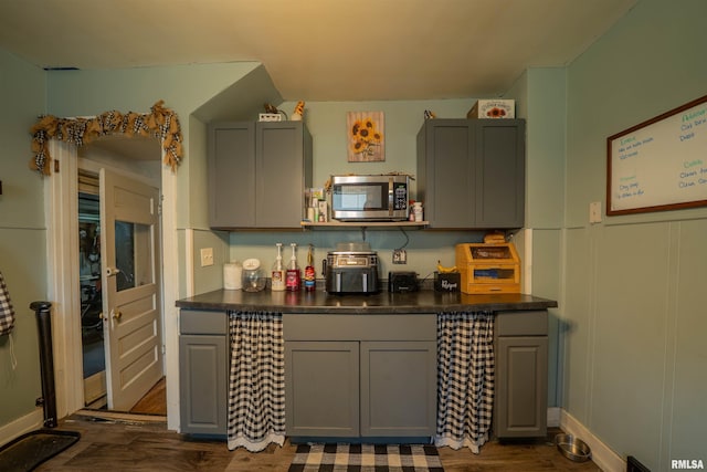 kitchen with stainless steel microwave, gray cabinets, dark countertops, and dark wood-style flooring