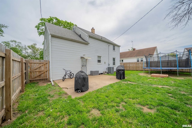 rear view of property with a trampoline, a patio area, central air condition unit, and a gate