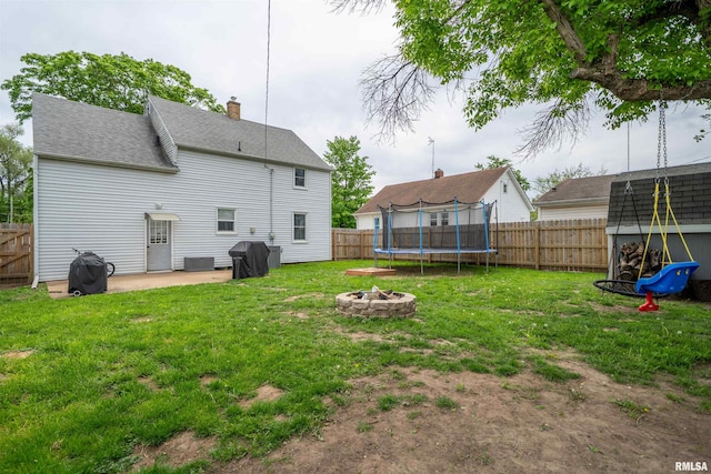 back of property featuring a trampoline, a patio, a chimney, a fire pit, and roof with shingles