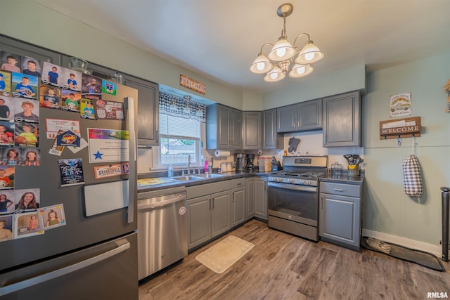kitchen featuring appliances with stainless steel finishes, a sink, gray cabinetry, dark countertops, and wood finished floors