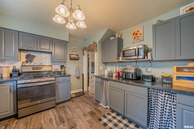 kitchen with appliances with stainless steel finishes, dark countertops, gray cabinets, a chandelier, and wood finished floors