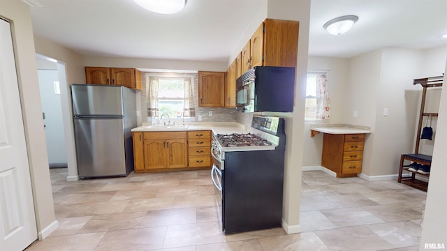 kitchen with appliances with stainless steel finishes, a sink, light countertops, brown cabinets, and baseboards