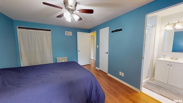 bedroom with light wood finished floors, a sink, ceiling fan, baseboards, and ensuite bath