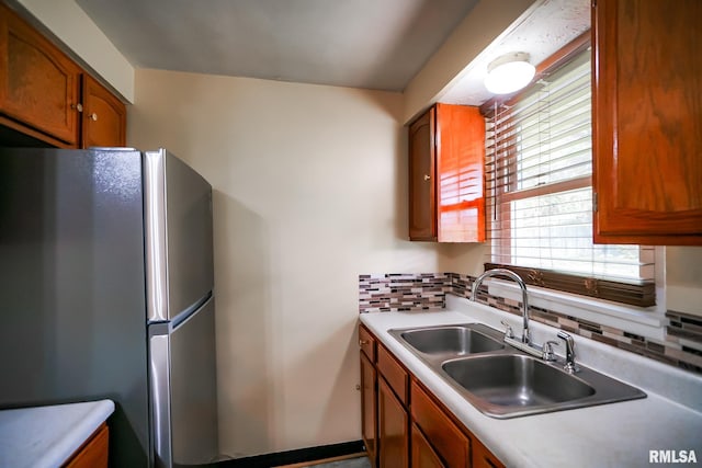kitchen with freestanding refrigerator, decorative backsplash, brown cabinetry, and light countertops