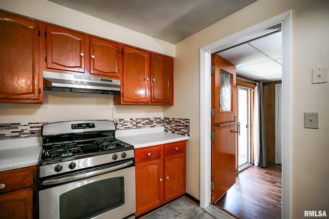 kitchen with stainless steel gas range oven, under cabinet range hood, light countertops, backsplash, and brown cabinets