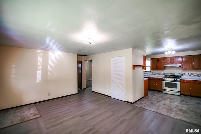 kitchen with stainless steel gas range oven, under cabinet range hood, wood finished floors, light countertops, and baseboards