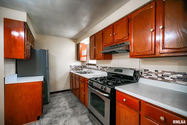 kitchen with under cabinet range hood, appliances with stainless steel finishes, a sink, tasteful backsplash, and light countertops