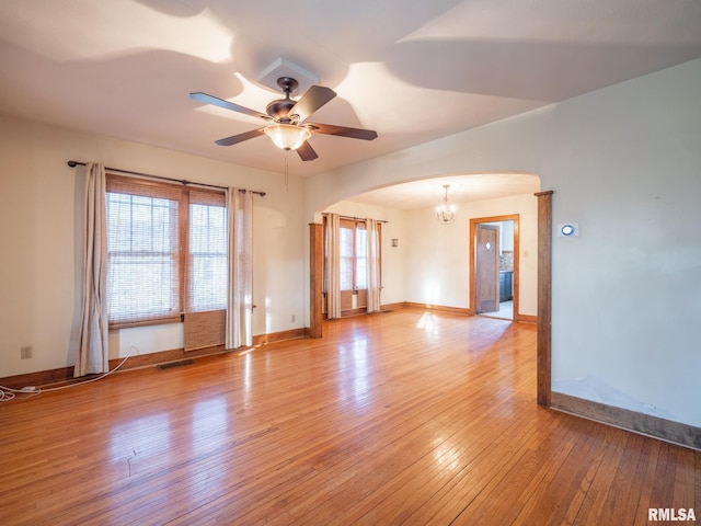 unfurnished room featuring arched walkways, a chandelier, light wood-type flooring, baseboards, and a ceiling fan