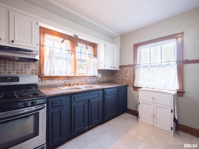 kitchen with stainless steel gas range oven, a sink, under cabinet range hood, blue cabinetry, and white cabinetry