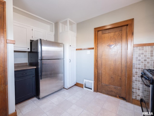 kitchen with freestanding refrigerator, white cabinetry, and gas range