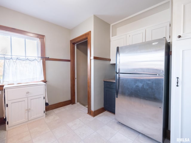 kitchen with freestanding refrigerator, white cabinets, and baseboards
