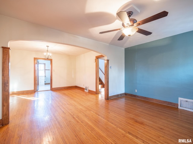 empty room with arched walkways, light wood finished floors, a ceiling fan, and stairs