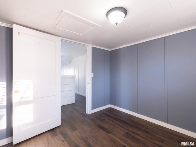 unfurnished bedroom featuring attic access, dark wood-type flooring, a decorative wall, and baseboards