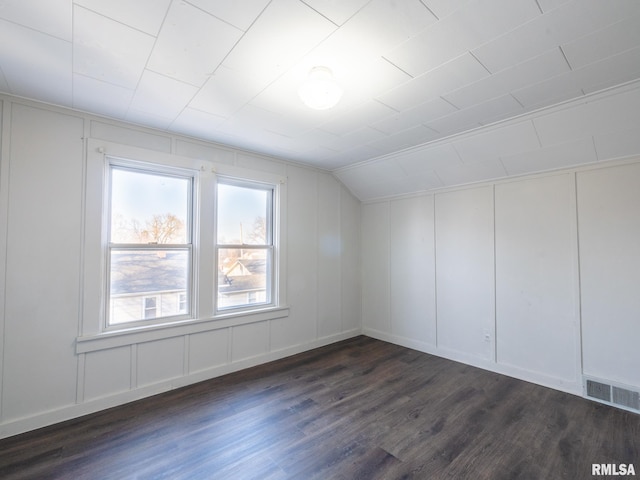 additional living space featuring lofted ceiling, dark wood-style floors, and a decorative wall