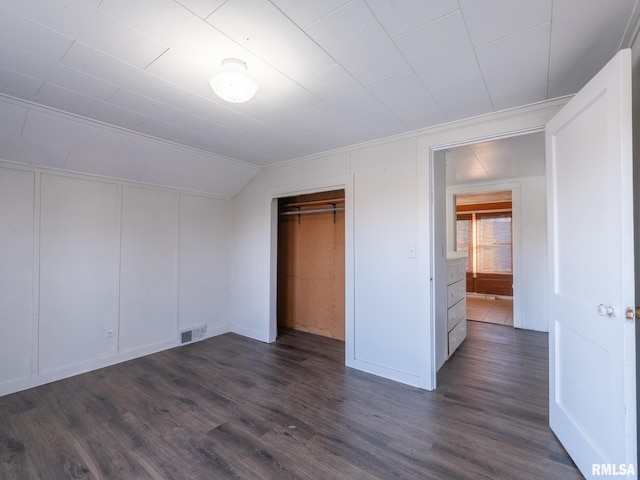 unfurnished bedroom with dark wood-style floors, vaulted ceiling, a decorative wall, and a closet