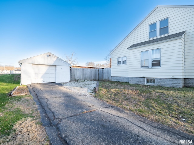 view of property exterior featuring fence, asphalt driveway, a detached garage, an outbuilding, and a shingled roof