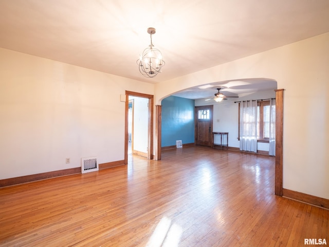 empty room with arched walkways, ceiling fan, light wood finished floors, baseboards, and a chandelier
