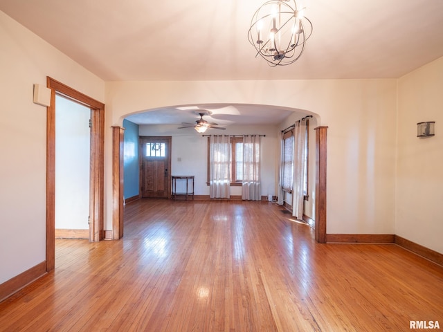 unfurnished living room featuring arched walkways, baseboards, a ceiling fan, light wood-type flooring, and a chandelier