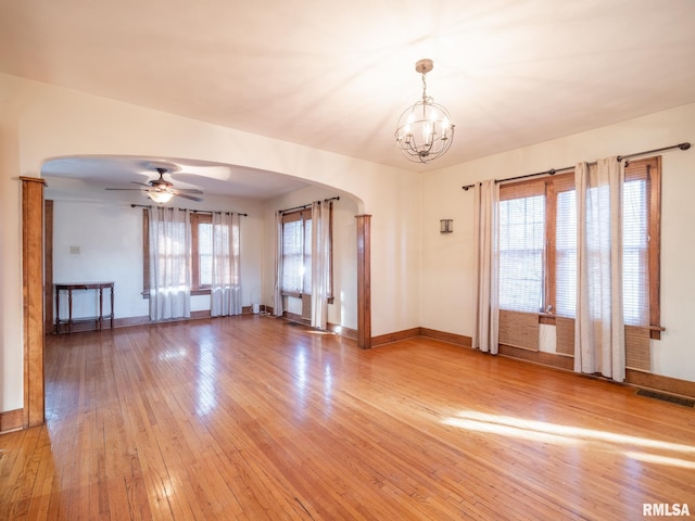 empty room with arched walkways, light wood-style floors, and baseboards