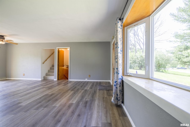 unfurnished living room with plenty of natural light, stairs, baseboards, and wood finished floors