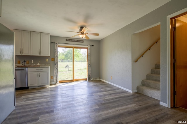 unfurnished dining area with dark wood-style floors, stairs, a ceiling fan, and baseboards