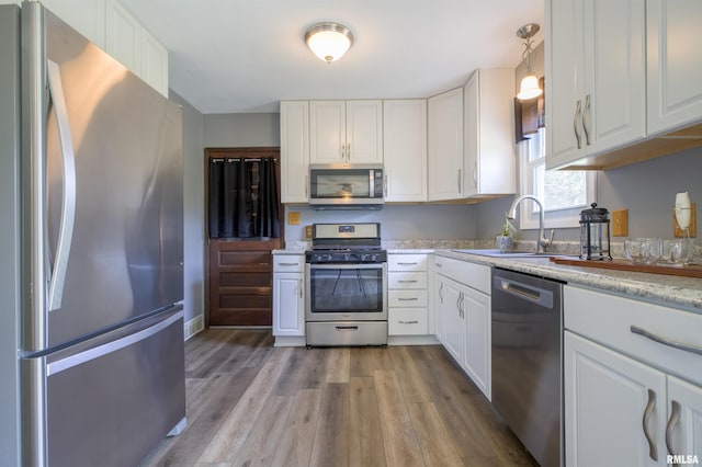 kitchen with appliances with stainless steel finishes, a sink, wood finished floors, and white cabinets