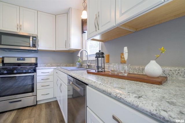 kitchen featuring appliances with stainless steel finishes, a sink, white cabinetry, and wood finished floors