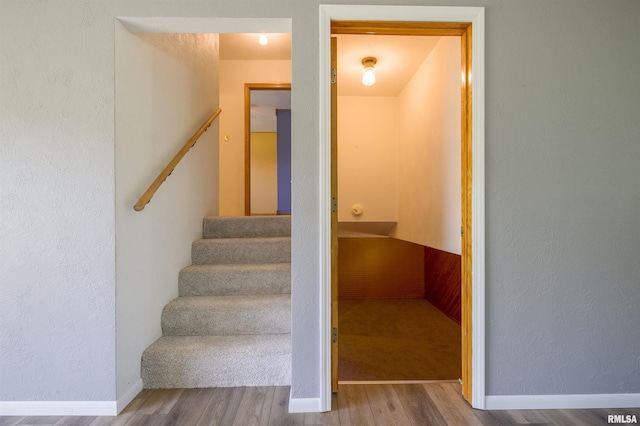 staircase featuring wood finished floors, a textured wall, and baseboards