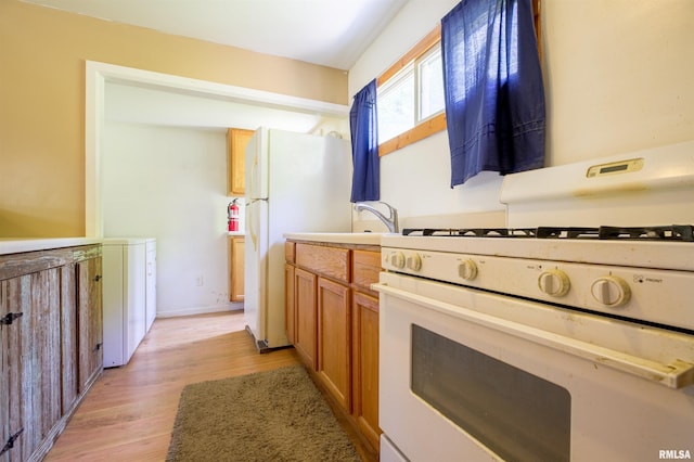kitchen featuring white appliances, light wood finished floors, brown cabinets, light countertops, and washer / dryer