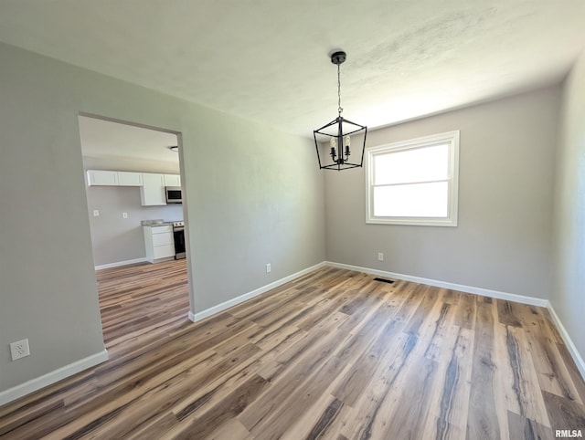 unfurnished dining area with a chandelier, baseboards, and wood finished floors