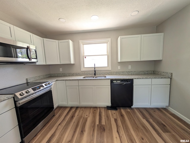 kitchen featuring appliances with stainless steel finishes, a sink, light wood-style flooring, white cabinets, and a textured ceiling