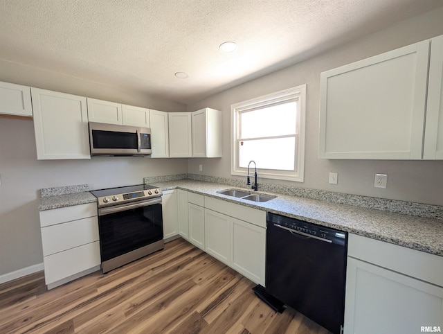 kitchen with stainless steel appliances, a sink, light wood finished floors, white cabinetry, and a textured ceiling
