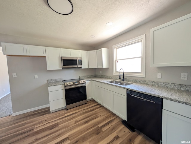 kitchen featuring stainless steel appliances, a sink, a textured ceiling, white cabinets, and light wood finished floors