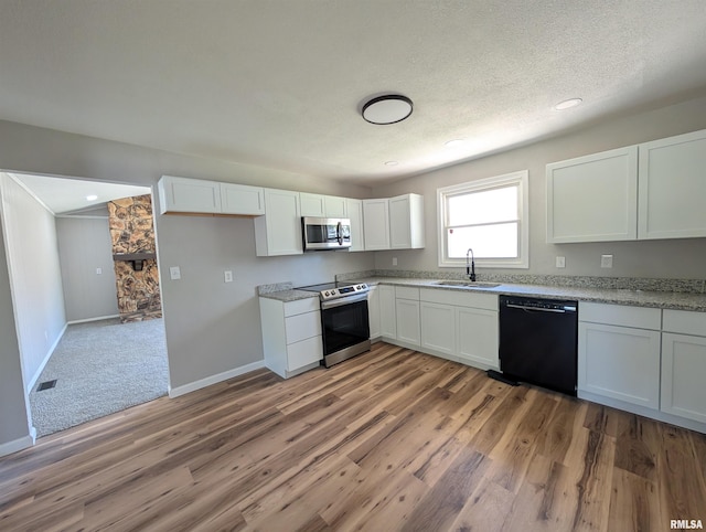 kitchen with stainless steel appliances, a sink, light wood-type flooring, white cabinets, and a textured ceiling