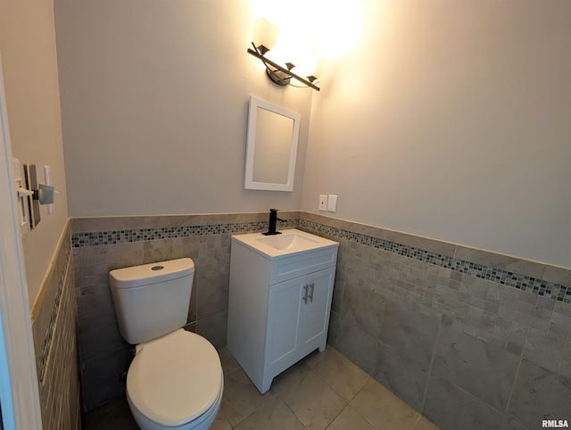 half bath with tile walls, a wainscoted wall, toilet, and vanity