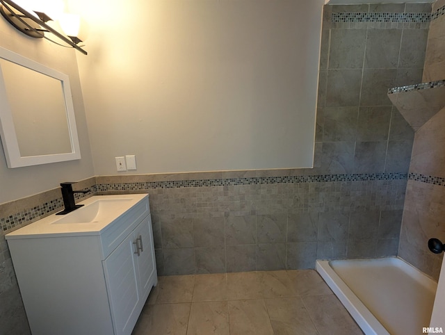 full bath featuring tile walls, vanity, tiled shower, tile patterned floors, and a wainscoted wall