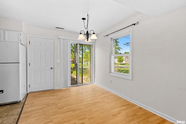 unfurnished dining area with a chandelier, light wood finished floors, and baseboards