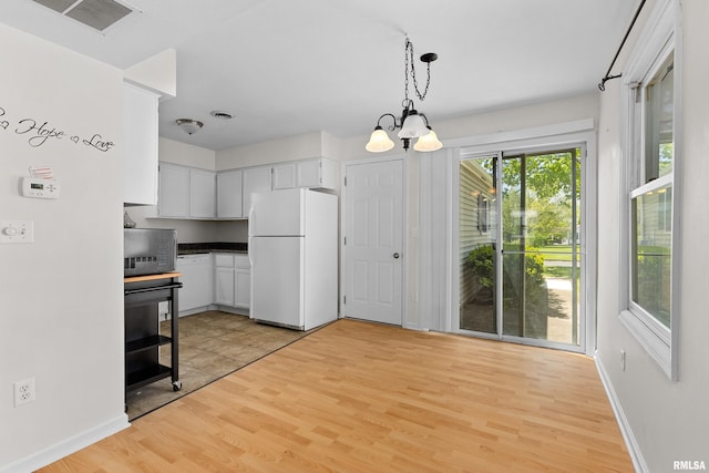 kitchen featuring freestanding refrigerator, a chandelier, light wood-style floors, dark countertops, and decorative light fixtures