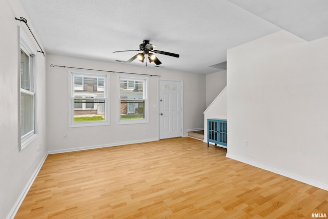 unfurnished living room with light wood finished floors, a ceiling fan, baseboards, and a textured ceiling