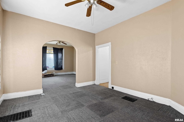 carpeted spare room with ceiling fan, arched walkways, and baseboards