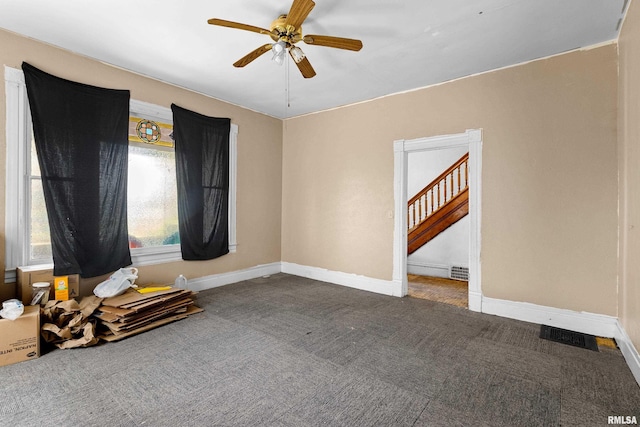 carpeted spare room featuring a ceiling fan, baseboards, and stairs