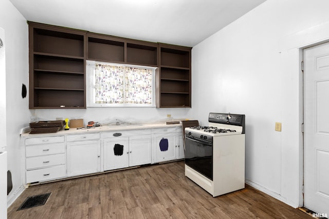 kitchen with white gas range, open shelves, wood finished floors, light countertops, and white cabinetry