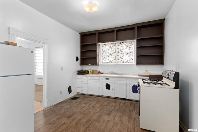 kitchen with freestanding refrigerator, range with gas stovetop, open shelves, and wood finished floors