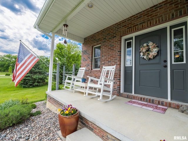 view of exterior entry with a porch, brick siding, and a lawn