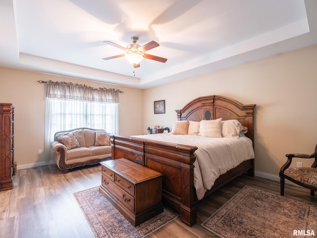 bedroom featuring a tray ceiling, light wood-style flooring, and baseboards