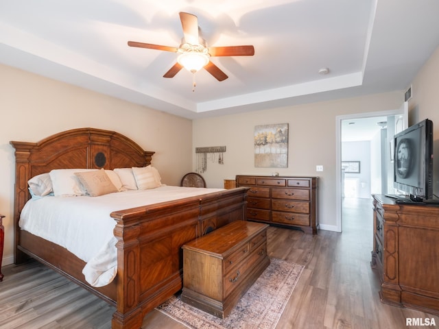 bedroom featuring a tray ceiling, wood finished floors, ceiling fan, and baseboards