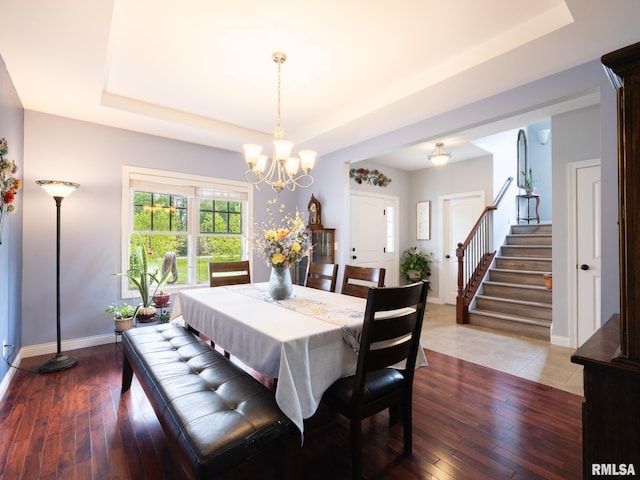 dining space featuring a tray ceiling, a chandelier, baseboards, and stairs