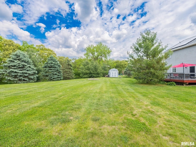 view of green lawn with a storage shed, a deck, and an outbuilding