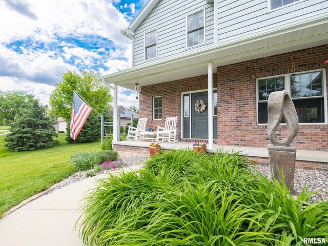 doorway to property featuring covered porch, a yard, and brick siding