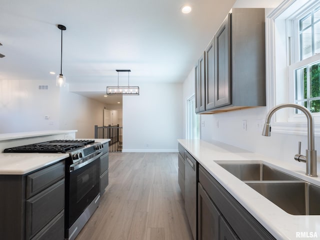 kitchen featuring stainless steel appliances, a sink, light wood finished floors, hanging light fixtures, and recessed lighting